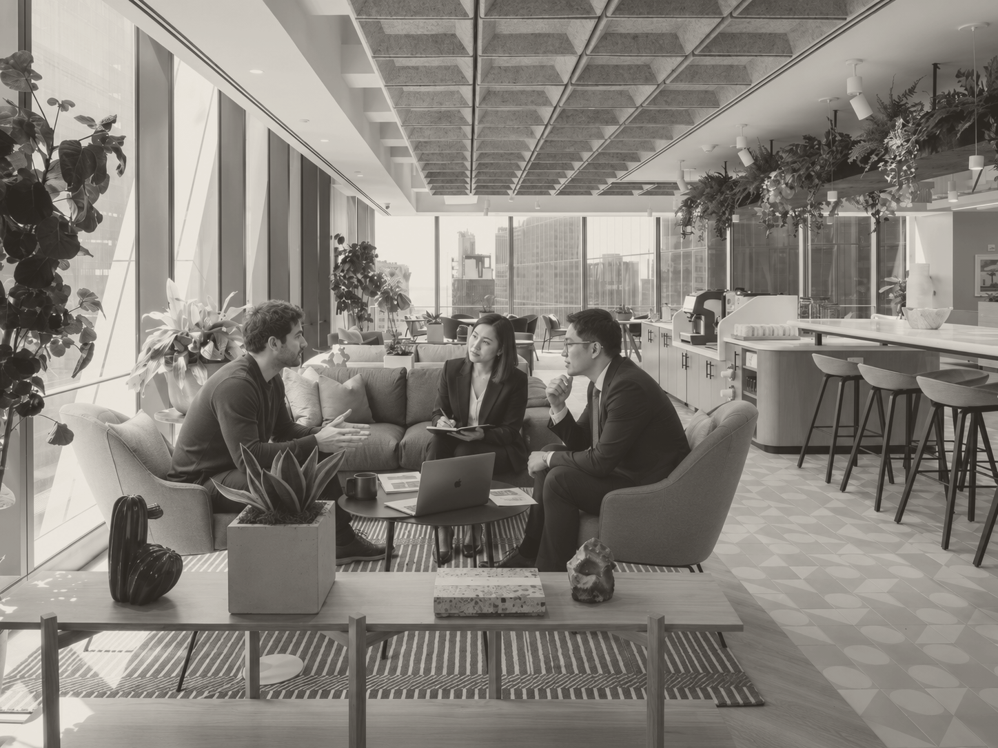 Three people in conversation in a light-filled Lower Manhattan office lounge with a laptop and printed figures on the table